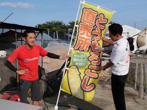 とうもろこし直売所とプリントされたのぼり旗を手にする市長