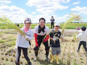 刈った稲を持った参加家族と記念撮影をする市長