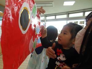 赤いこいのぼりに手形を貼る女の子の写真。