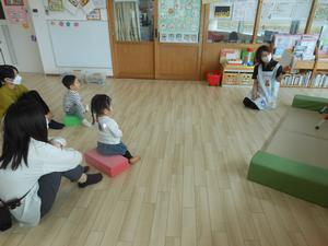 絵本の読み聞かせをスポンジ積み木に座って見ている子ども達の様子