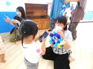 完成した作品を持つママをスマホで撮影する女の子の様子