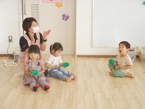 3人のお友だちがかえるのパペットを持ち、みんなで「かえるのうた」をうたっている様子