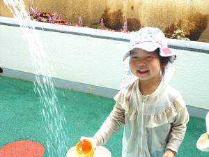 じょうろのお水を嬉しそうにカップに入れようとする女の子の写真