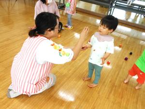 アシスタントの先生が男の子にお手玉を渡している様子