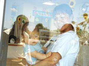 お部屋の中から水遊びの様子を見ている赤ちゃん親子の写真