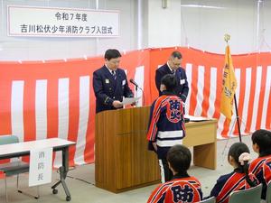 入団通知を壇上で読み上げる消防長とそれを聞くクラブ員