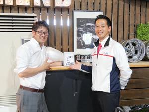 市長が描いた似顔絵を挟んで市長と社長の記念撮影