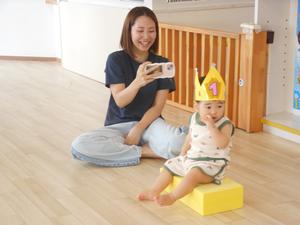 スポンジ積み木に座る誕生児の男の子とその様子を写真撮影するママの様子