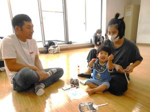 クレヨンを両手に持って笑う男の子と見守るママとおじいちゃんの様子