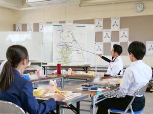 市域図を指示棒で指して説明をする市長