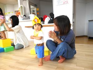 冠を被ってカメラに目を向ける誕生児の女の子と拍手するママの写真