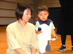 新聞を丸めて作ったおにぎりを両手に持つ男の子と見守るママの写真