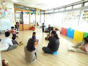 絵本をの読み聞かせをしている保育士とそれを見ている親子達の様子