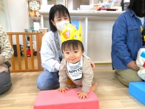 カラー積み木に登ろうとしている誕生児の男の子と支えているママの様子
