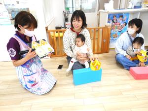 ママの膝に座っている女の子と誕生日カードを紹介している保育士の様子