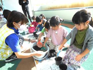 場保育士が持つバケツの土をシャベルですくっている子ども達の様子