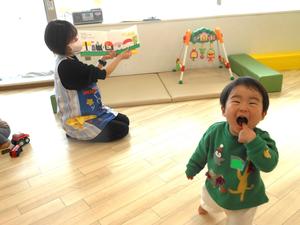 絵本を読む保育士とカメラに向かって笑顔を見せる男の子の様子