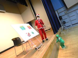 ステージの上でパネルシアターをやっている保育士とそれを見ている女の子の様子