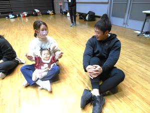 ママの膝に座っている女の子とそれを見ているパパの様子