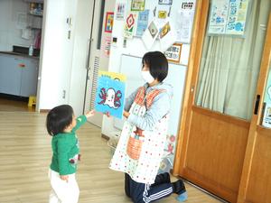 紙芝居を読む保育士と近づいて指差しする男の子の様子