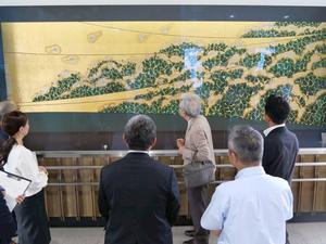 吉川美南駅の室瀬先生の作品である蒔絵の前で話をする様子