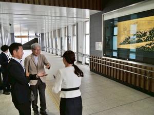 吉川美南駅の室瀬先生の作品である蒔絵の前で話をする様子