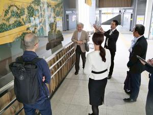 吉川美南駅の室瀬先生の作品である蒔絵の前で話をする様子
