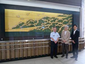 吉川美南駅の室瀬先生の作品である蒔絵の前で記念撮影をする室瀬先生、駅長、市長