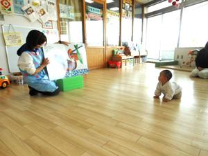 大型絵本『月ようびはなにたべる？』を読む保育士と四つん這いで見ている赤ちゃん様子