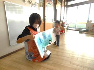 保育士が読んでいる大型絵本をめくろうとしている男の子の様子