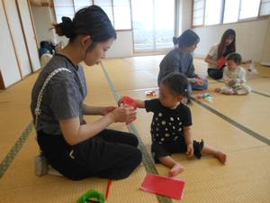 ちょうちょ製作で子どもが丸めたお花紙を母が持つ袋に入れようとしている様子