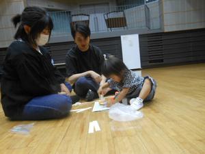 ヘビの工作でのりを使っている2才の子どもとその様子を見守っている両親