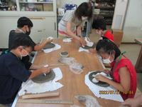 土を型にはめて皿のかたちに整える参加者と指導する吉川市陶芸協会の会員