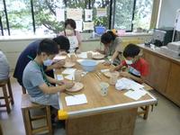 絵付けの下書きを行う参加者と見守る吉川市陶芸協会の会員