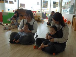 お膝の上で読み聞かせを見ている、2組の赤ちゃんとママ