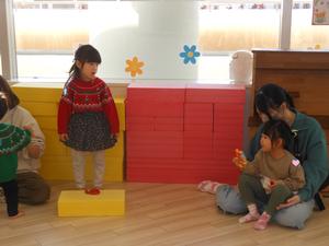 積み木の上で踊っている子と鈴で合奏している子の写真
