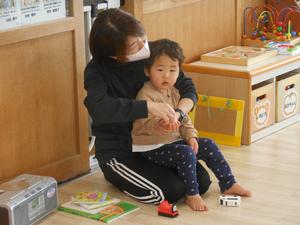 保育士が子どもを膝に座らせ「いっぽんばしこちょこちょ」をやっている写真