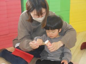 トイレットペーパーの芯に折り紙をのり付けする親子の写真