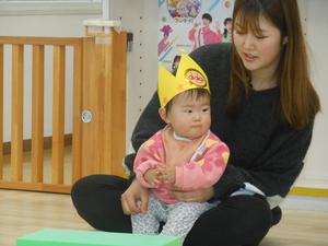 3人目のお誕生児が、ママの膝の上で拍手している様子