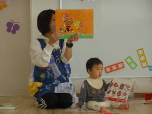 「アンパンマン」の紙芝居を読んでいる保育士の横で遊んでいる男の子の写真