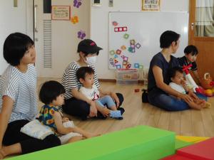 ママのお膝に座って読み聞かせを見ている写真